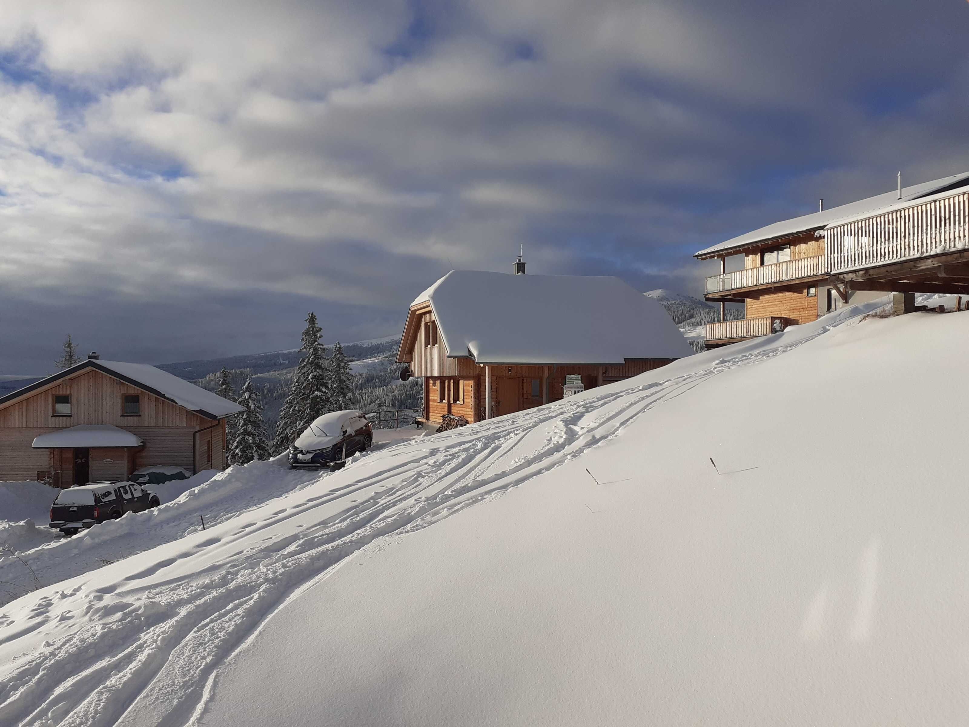 Eine Holzhütte mit schneebedecktem Dach, einer Holzdiele und einer Seilbahn im Hintergrund.