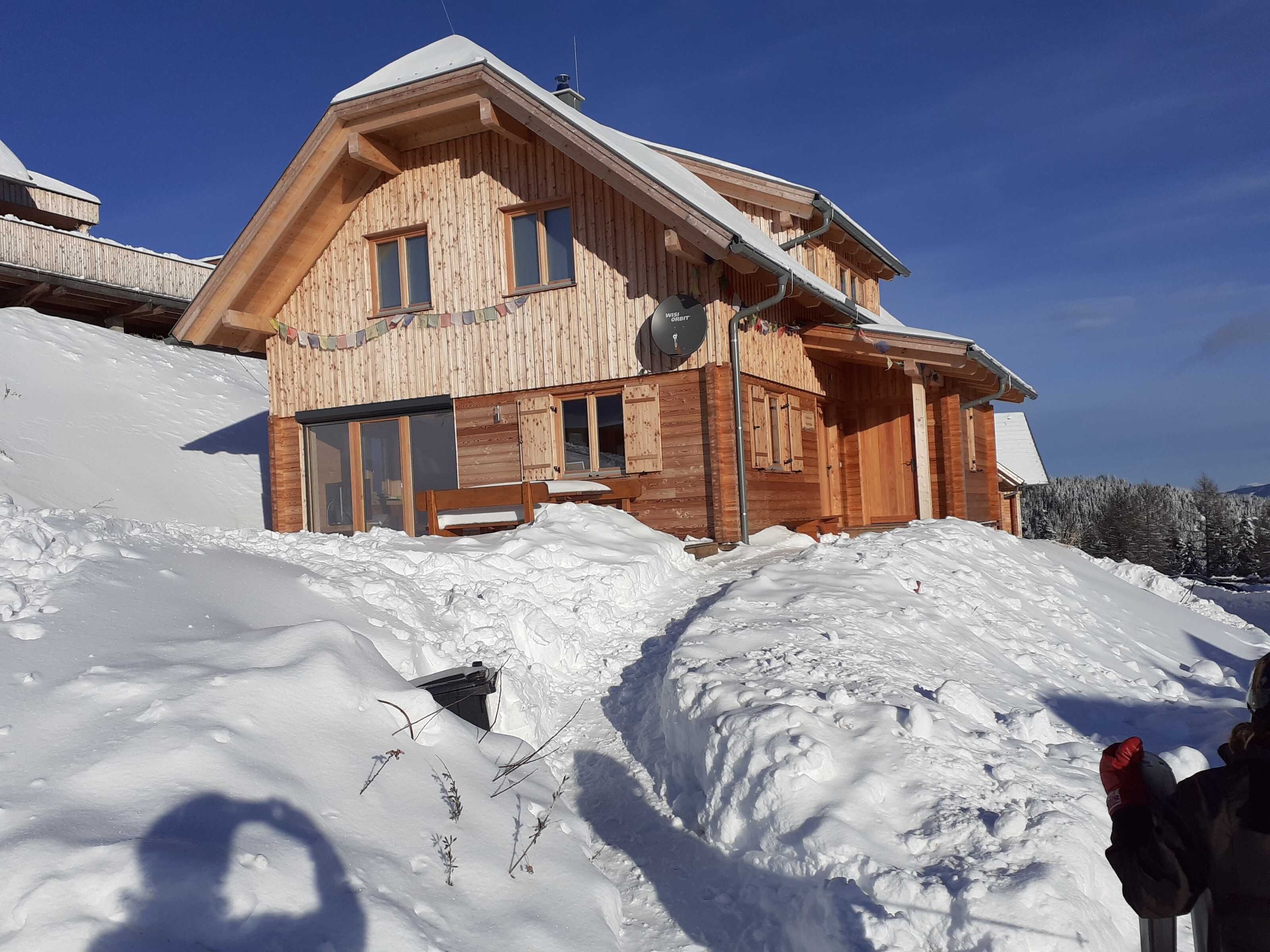 A wooden chalet with a sloped roof, large windows, and a snow-covered landscape.