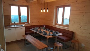 L’intérieur d’une cabane en bois comprend une cuisine, une table à manger, des bancs et trois fenêtres.