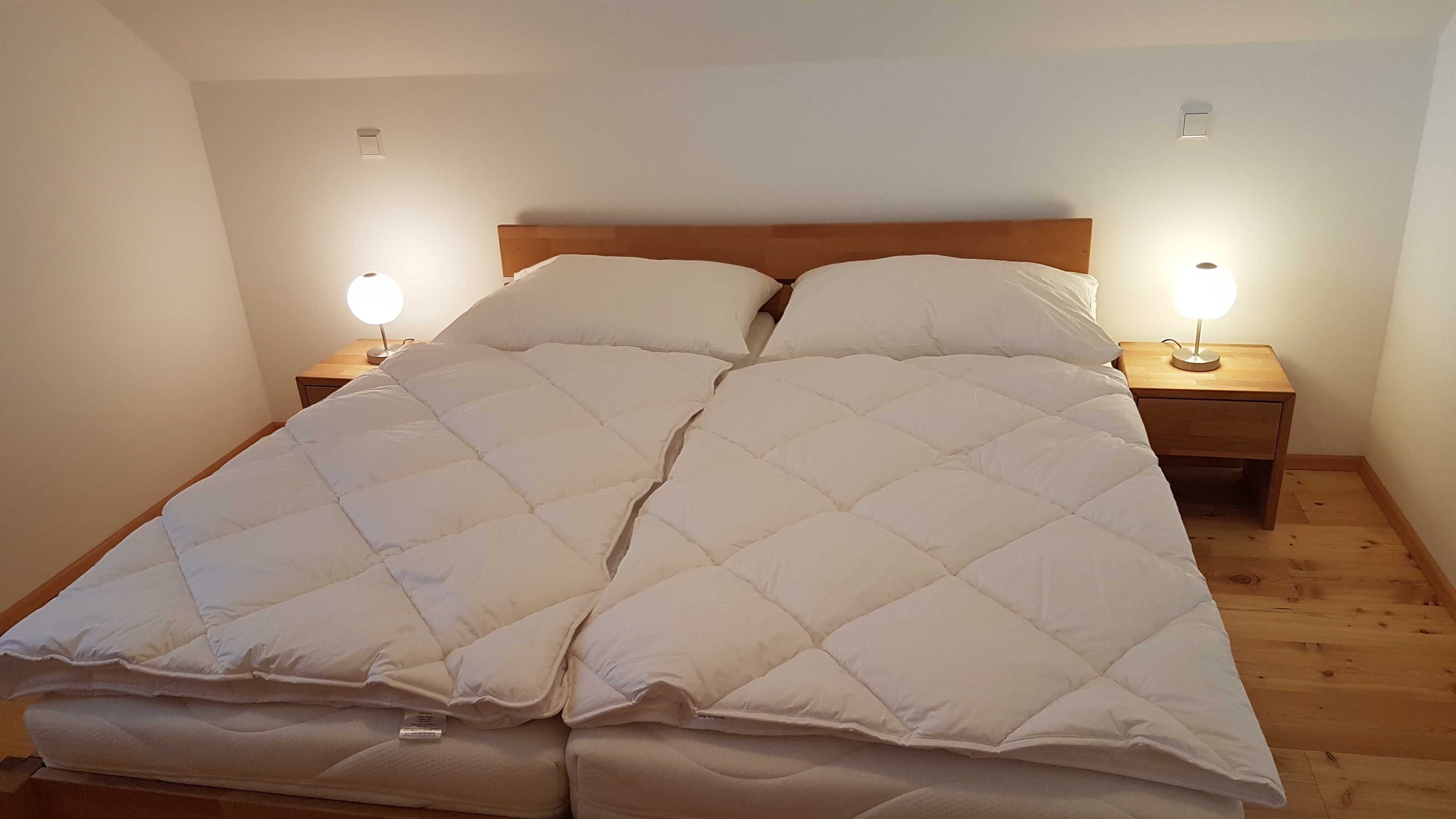 Un lit double avec une couette matelassée, deux tables de chevet avec des lampes et une tête de lit en bois.