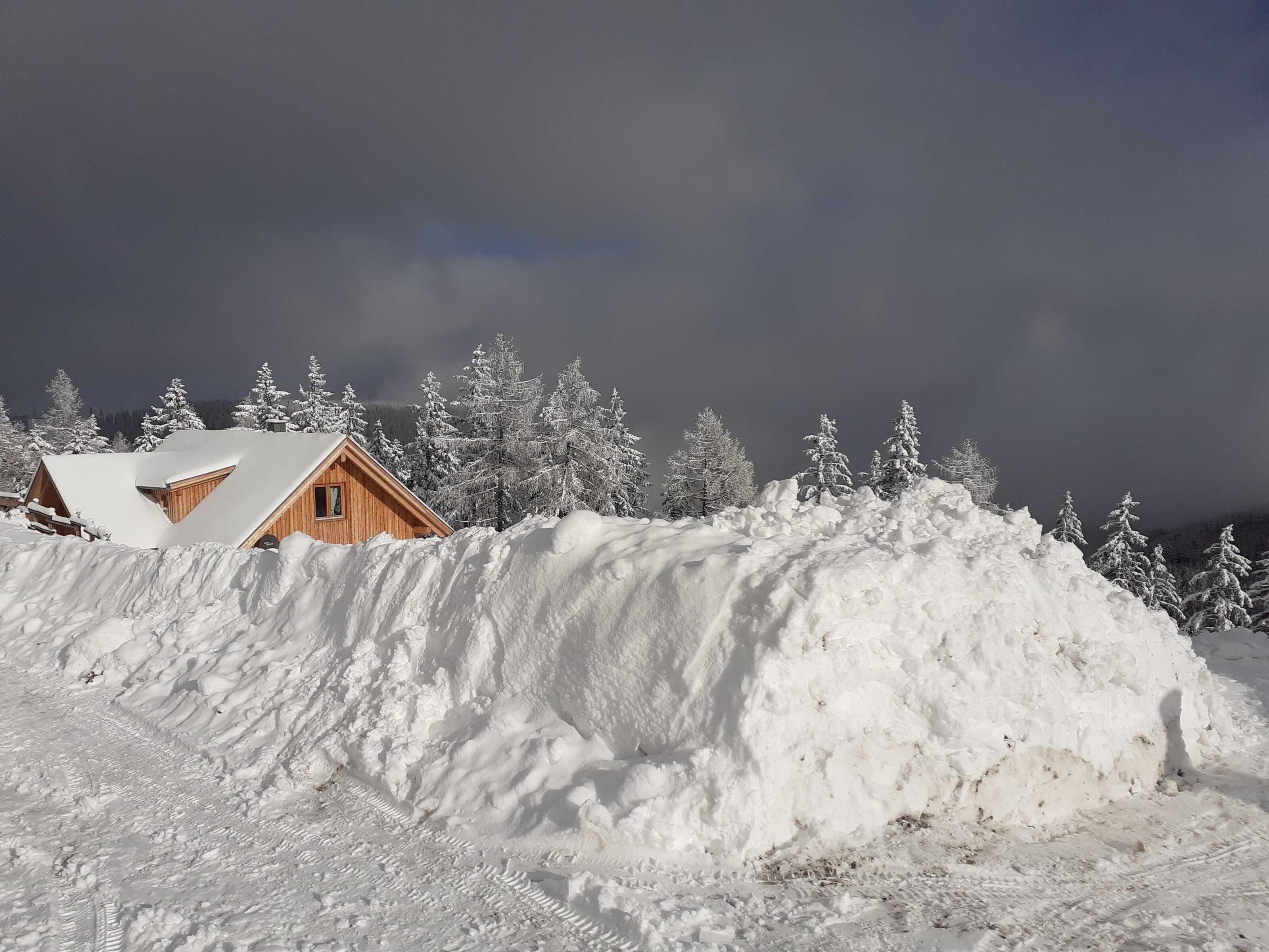 Une cabane en bois, dotée d’un toit en pente, entourée d’arbres couverts de neige et bordée d’une grande accumulation de neige.