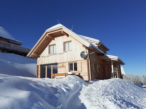 Puinen alppimaja, jossa on kalteva katto, suuret ikkunat ja satelliittiantenni.