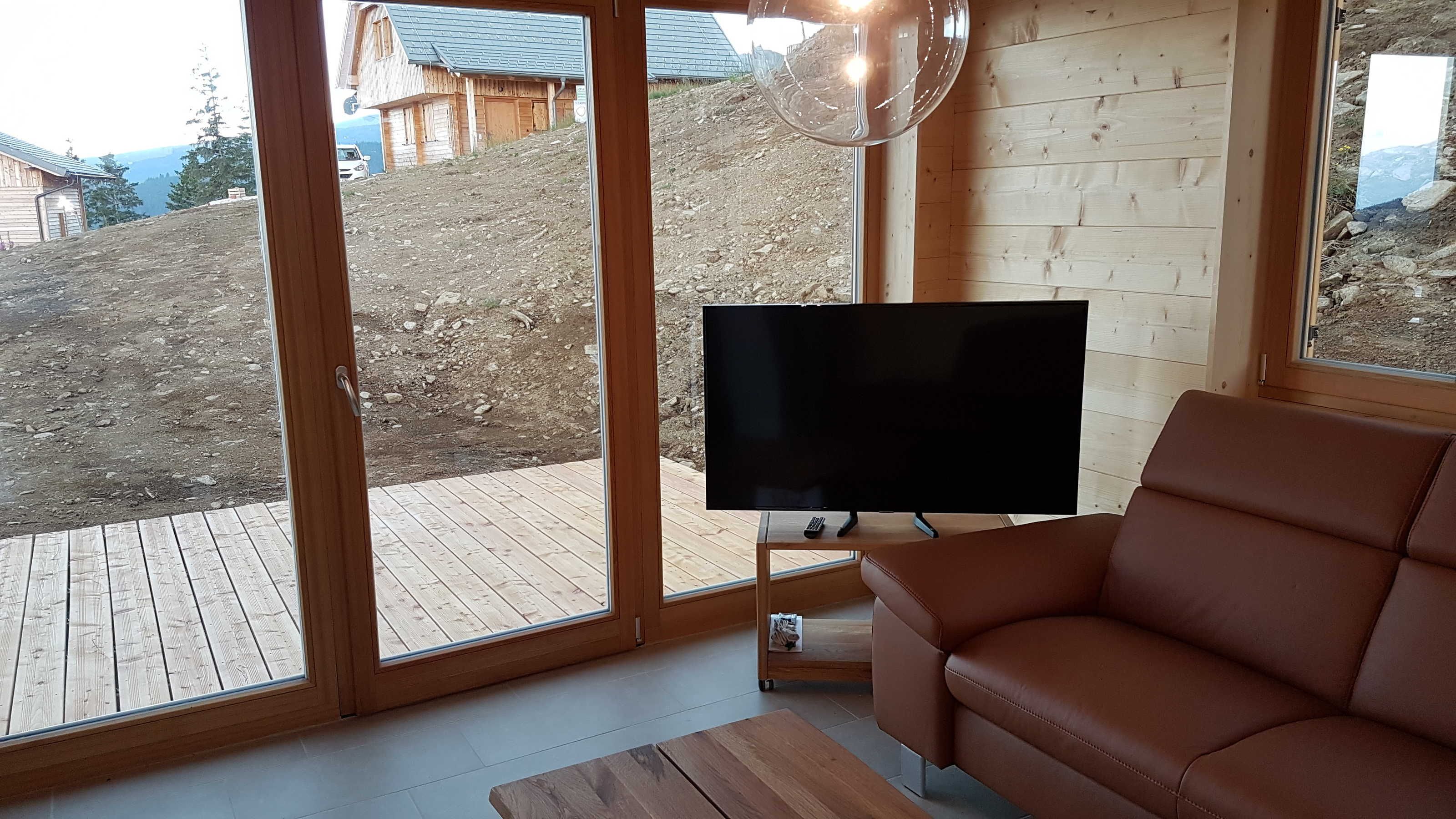 Un salon moderne doté d’un grand téléviseur, de meubles en bois et offrant une vue sur une région montagneuse.