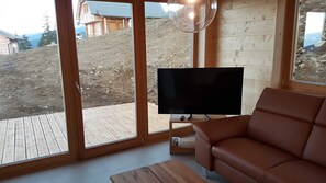 A modern living room with a large TV, wooden furniture, and a view of a mountainous area.