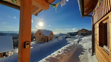 A wooden cabin with a snow-covered yard and a clear view of the surrounding mountains.