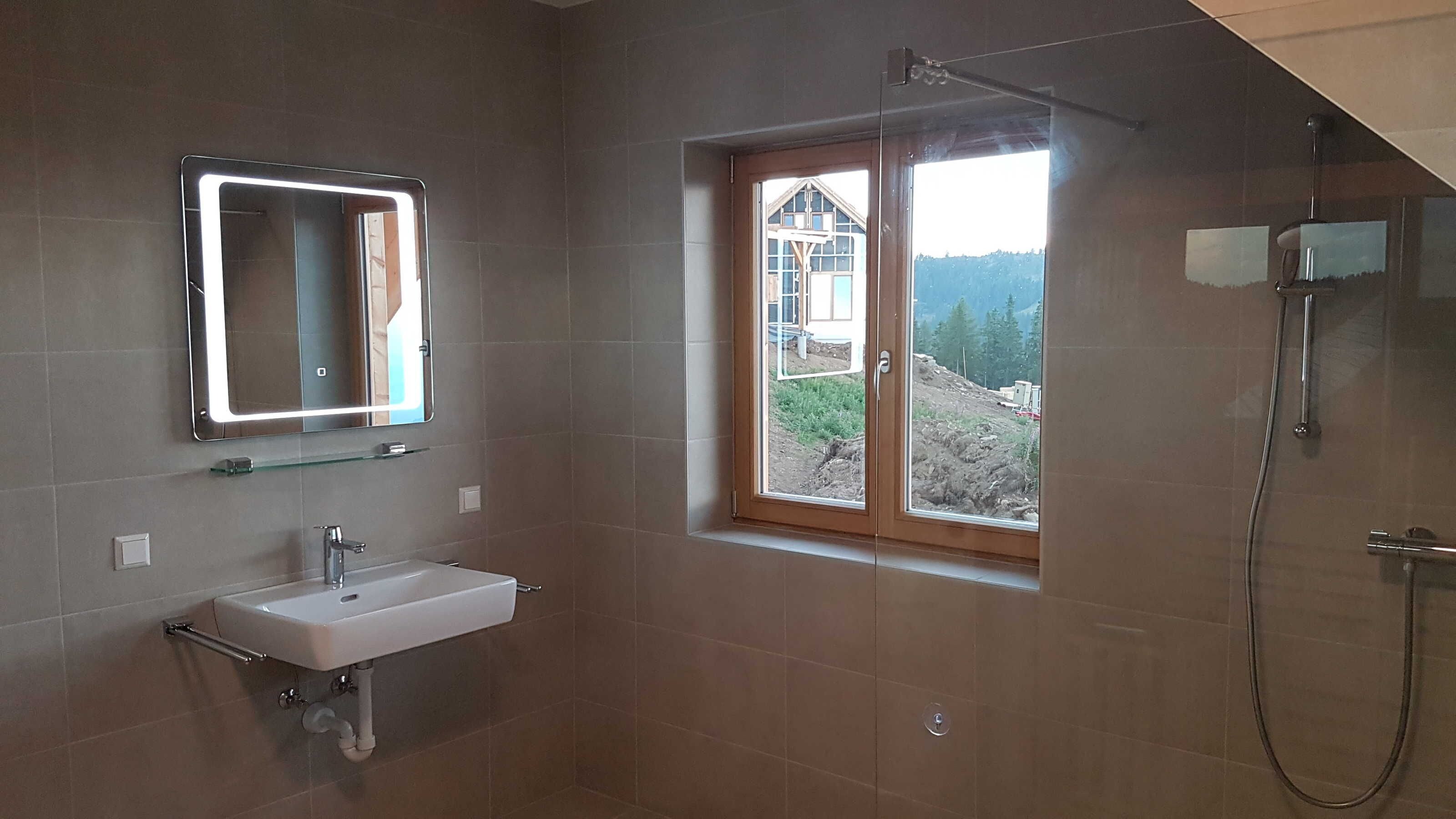 Une salle de bain avec un lavabo, un miroir, une douche et une fenêtre donnant sur un beau paysage.