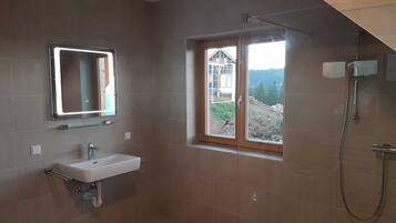 Une salle de bain avec un lavabo, un miroir, une douche et une fenêtre donnant sur un beau paysage.
