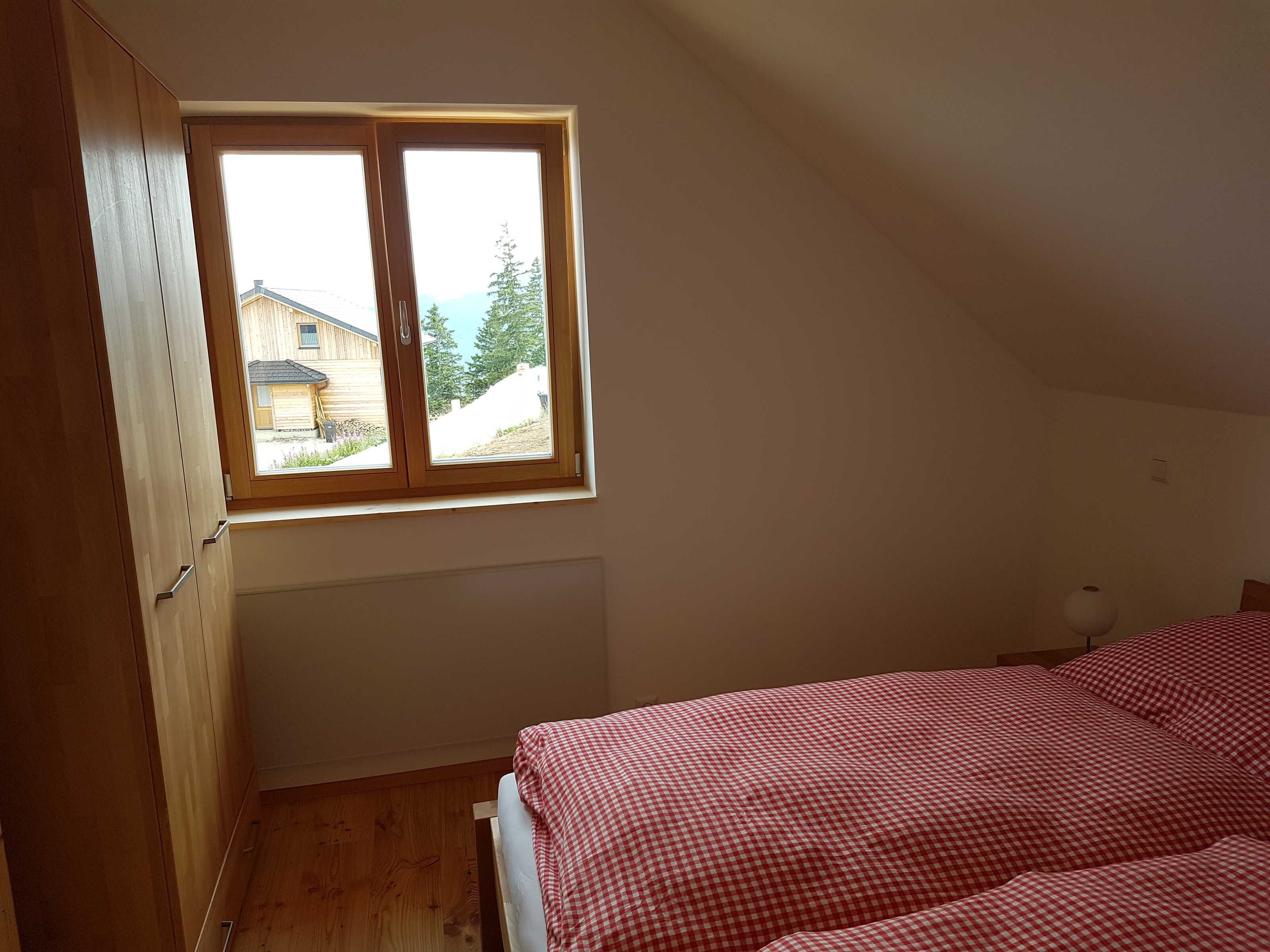 Ein Schlafzimmer mit Fenster, Holzschrank und einem Bett mit Karomuster-Bettwäsche.
