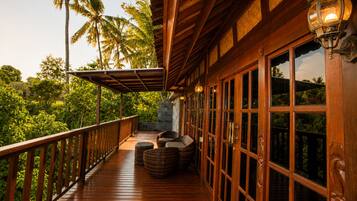 A wooden deck with a railing, wicker furniture, and a view of tropical vegetation.