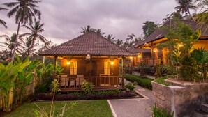 Ein Bungalow mit einem Ziegeldach, einer Veranda und einem Garten mit tropischen Pflanzen.