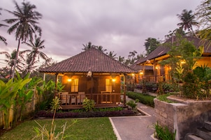 Una cabaña con techo de tejas, un porche y un jardín con plantas tropicales.
