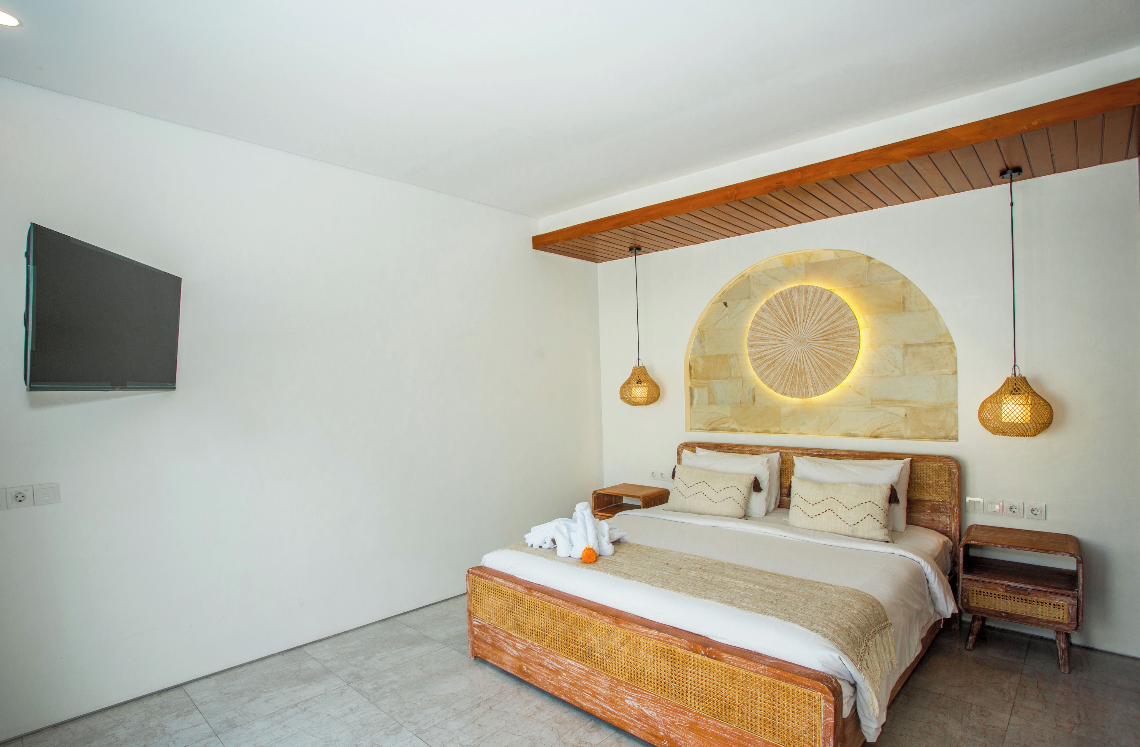 A bedroom with a bed, bedside tables, a wall-mounted TV, and a unique circular light fixture.