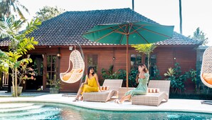 A poolside area with wicker lounge chairs, a hanging chair, and a large umbrella. - Villa Waturenggong Ubud (Ubud)