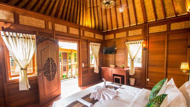 A wooden room with a bed, curtains, a desk, and a television. - Villa Waturenggong Ubud (Ubud)
