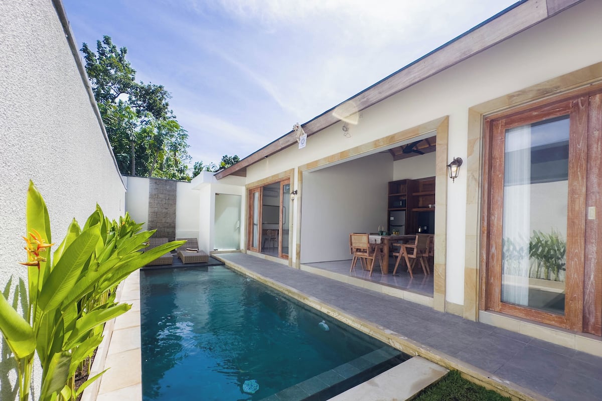 Una casa moderna con piscina, un patio con mobiliario exterior y un amplio ventanal corredera que da a un comedor.