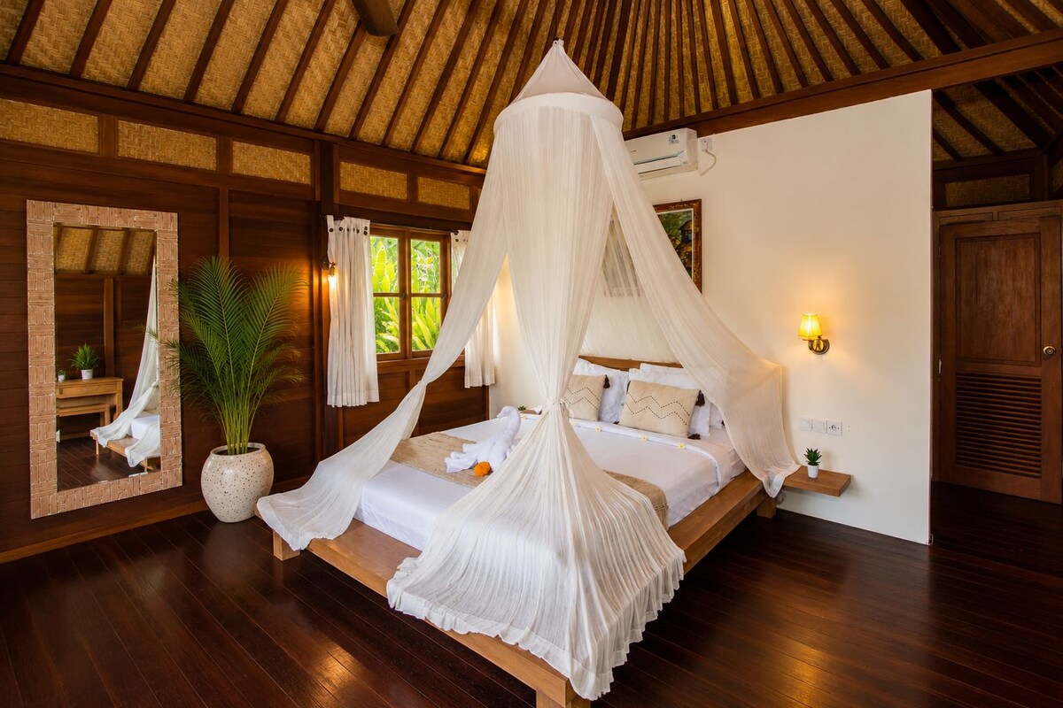 Une chambre à coucher avec un lit à baldaquin, un grand miroir, une plante en pot et une table de chevet avec une lampe.