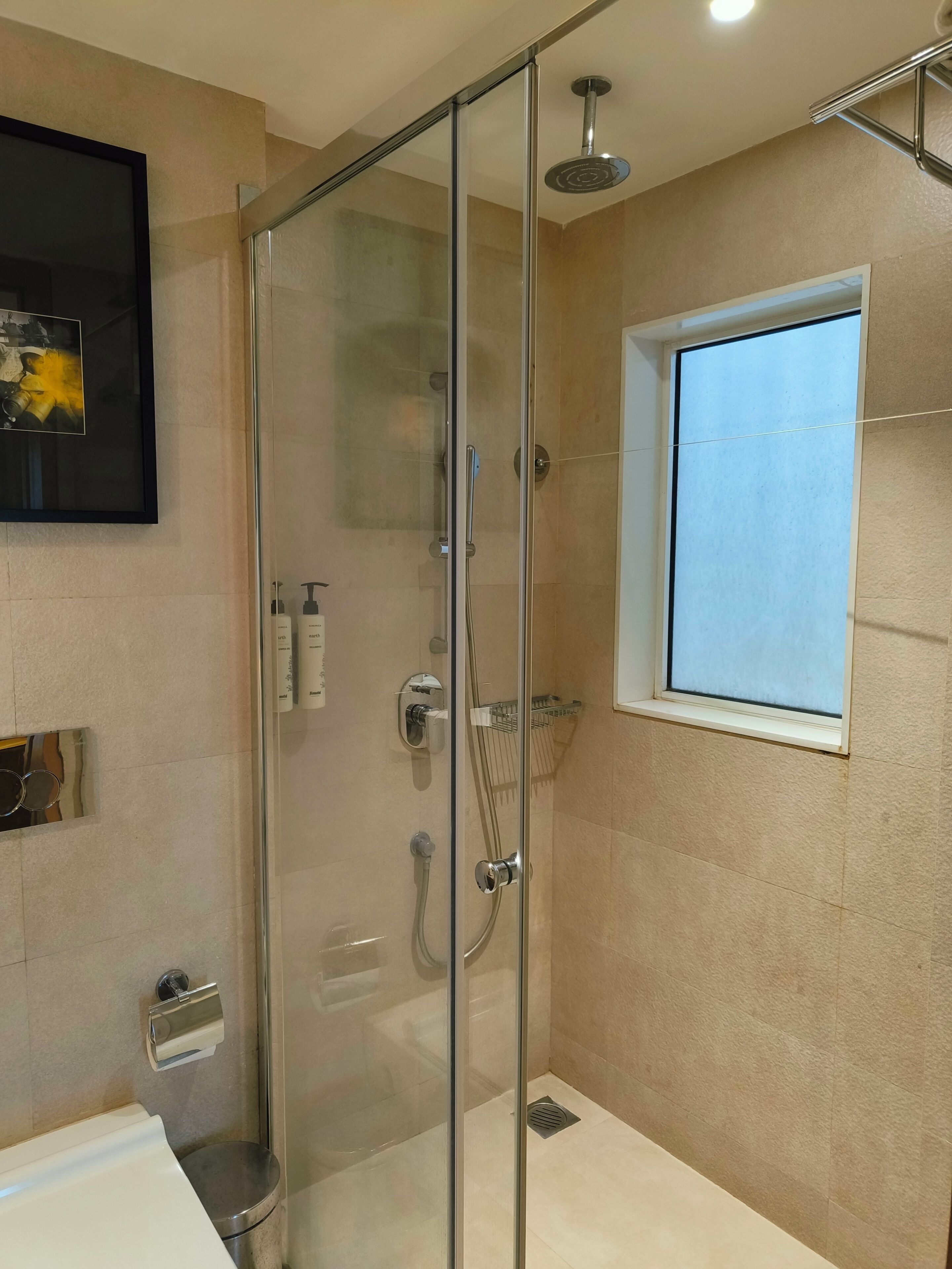 A modern bathroom with a glass-enclosed shower, a small window, and a mounted sink.