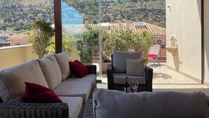 A balcony with a sofa, a chair, and a table with a bottle and glass.