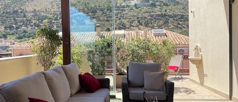 A balcony with a sofa, a chair, and a table with a bottle and glass.