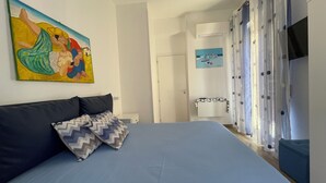 A bedroom with a bed, a painting, a wardrobe, and a bathroom visible through an open door.