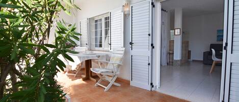 A room with a white tiled floor, a white table with chairs, and a potted plant.