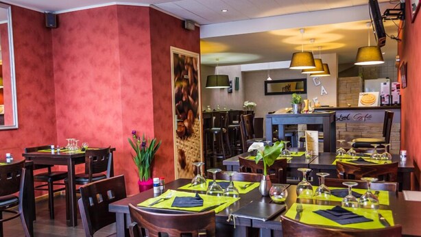 Ein Restaurant mit mehreren Tischen und Stühlen, an jedem Tisch eine grüne Tischdecke und Besteck.