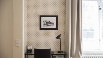 Una habitación con papel tapiz estampado, un cuadro en la pared, un escritorio con una lámpara y una silla.
