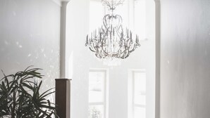 Una escalera con candelabro, plantas en macetas y grandes ventanales que dejan entrar luz natural.