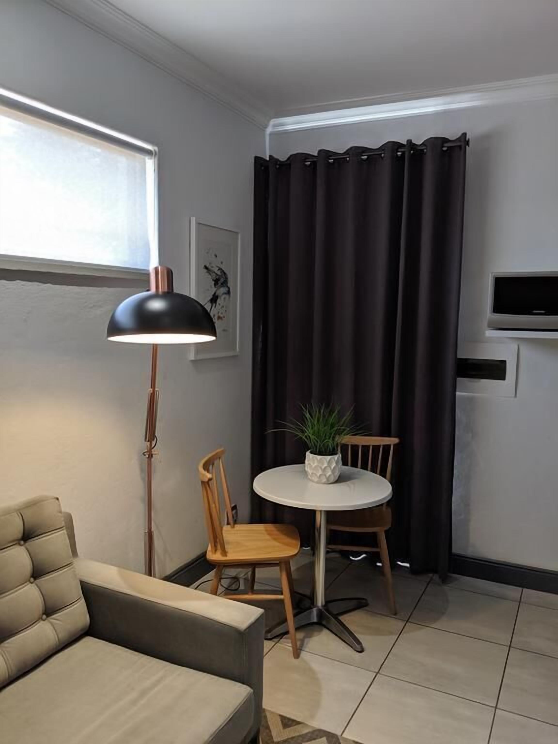 A compact living space with a sofa, a small round table with a potted plant, a floor lamp, and a TV mounted on the wall.