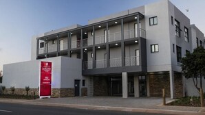 A modern building with a flat roof, multiple balconies, and a prominent red sign on the left. - Junction 502 Apartments (Pretoria)