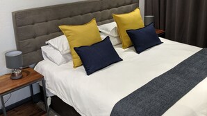 A neatly made bed with white bedding, two yellow and two navy blue pillows, a grey headboard, and a grey throw blanket. - Junction 502 Apartments (Pretoria)