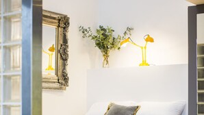Ett modernt sovrum med en säng, en spegel, en växt och en lampa.