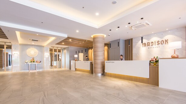 A modern hotel reception area with a marble floor, a reception desk, and a wall-mounted sign. - Madison Bangkok (Bangkok)