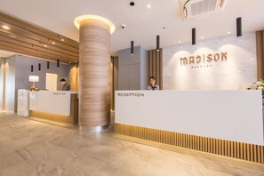 A reception area with a marble wall, a reception desk, and a large cylindrical column. - Madison Bangkok (Bangkok)
