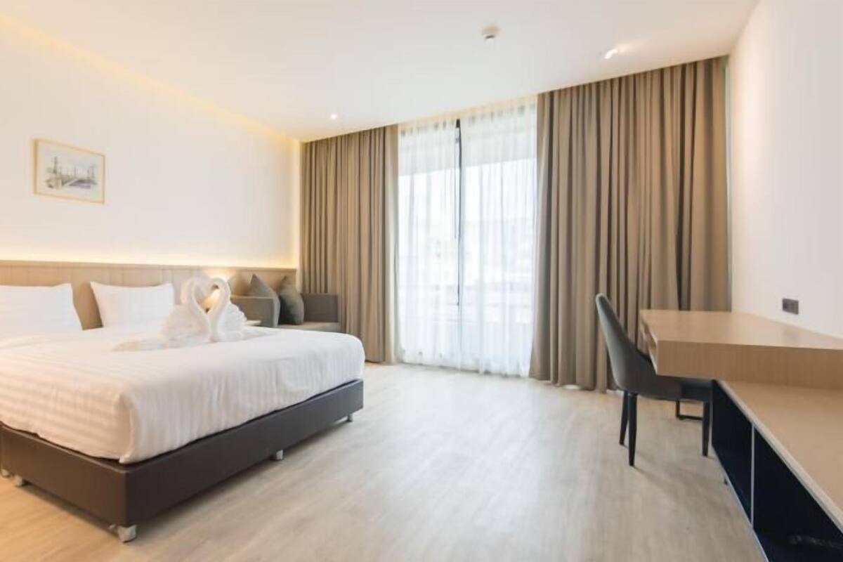 Una habitación de hotel moderna con una cama, un escritorio, una silla y un ventanal con cortinas.