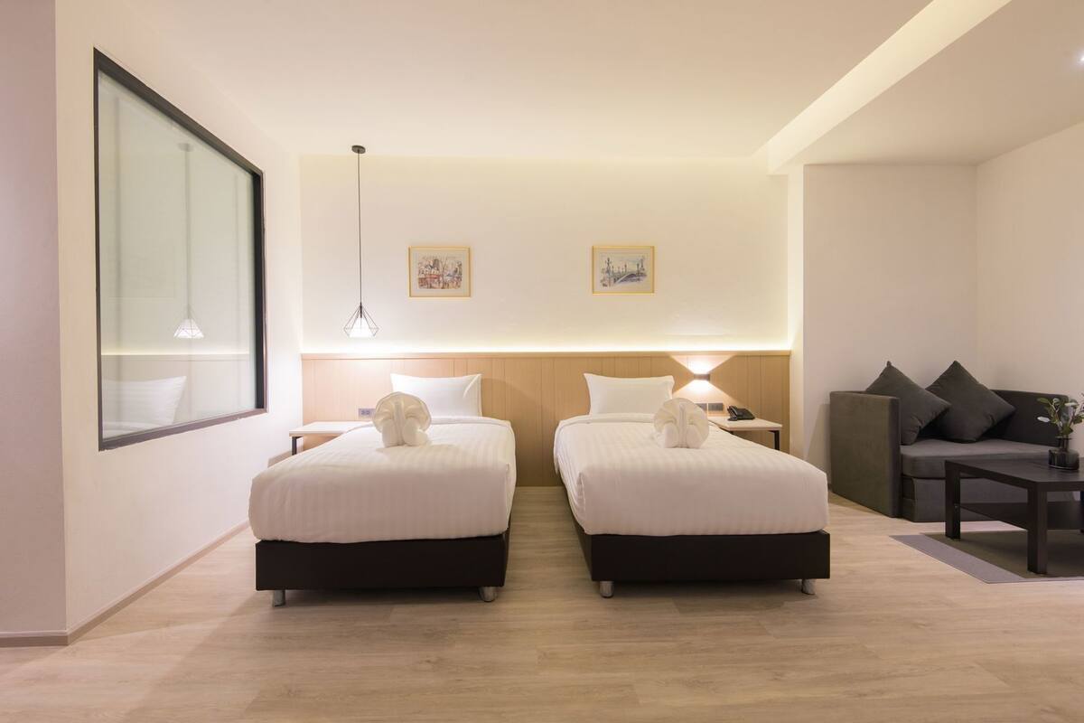 Habitación de hotel con dos camas, un sofá, una mesita y un ventanal grande.