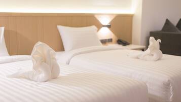A hotel room with two beds, each with a neatly folded towel and a lamp on the nightstand.