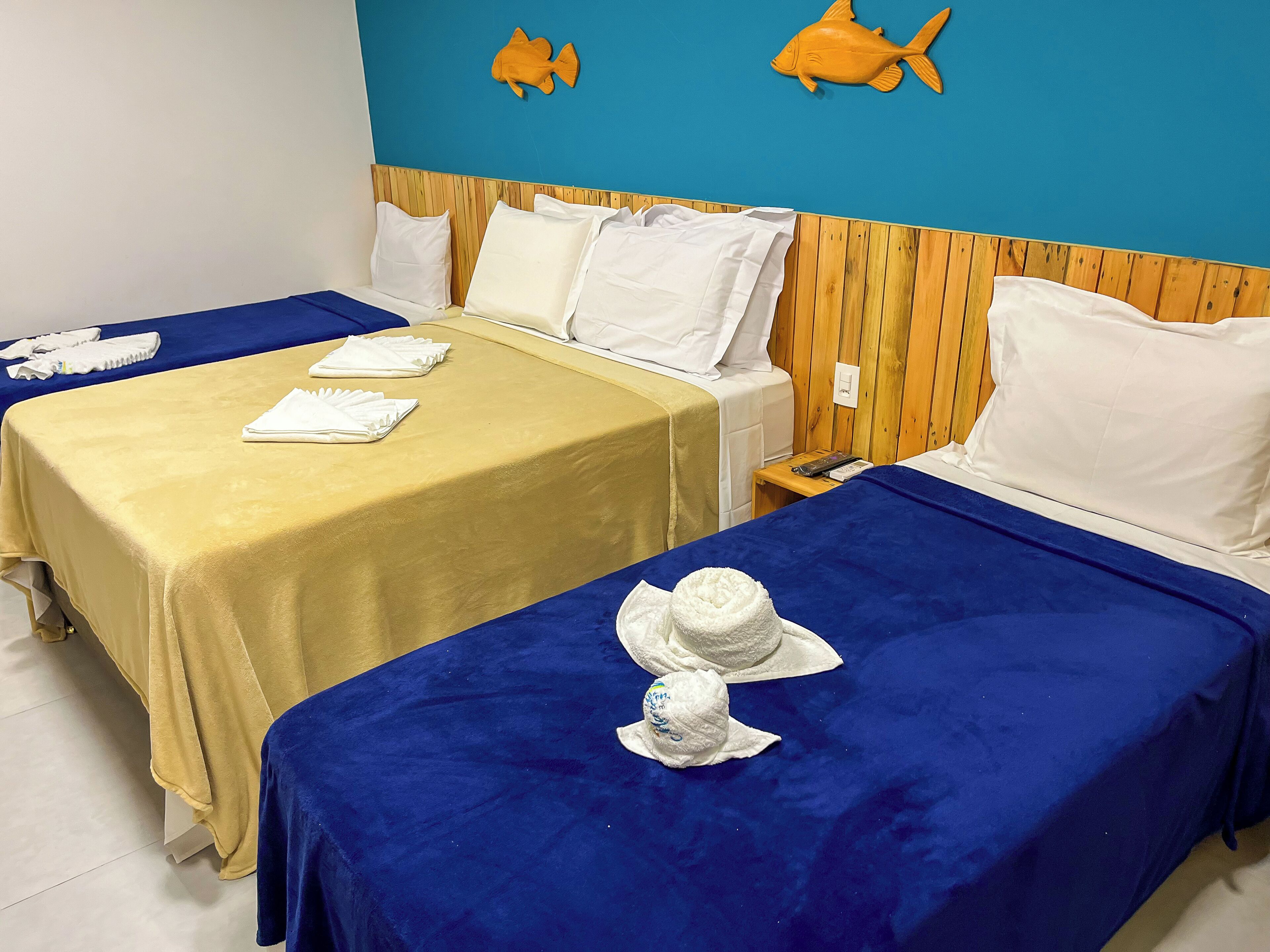 A hotel room with two beds, each with a blue and yellow bedspread, white pillows, and a white towel. There are wooden headboards and a blue wall with fish decorations.