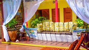 Un área de descanso frente a la playa con un toldo colorido, un letrero que dice "Pousada" y una terraza de madera.