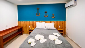 Habitación de hotel con cabecera de madera, cama con sábanas blancas y tres anclas en la pared azul.