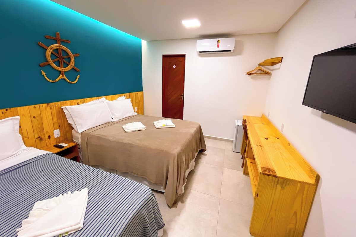 A hotel room with a bed, a desk, a TV, and a wall-mounted air conditioner.