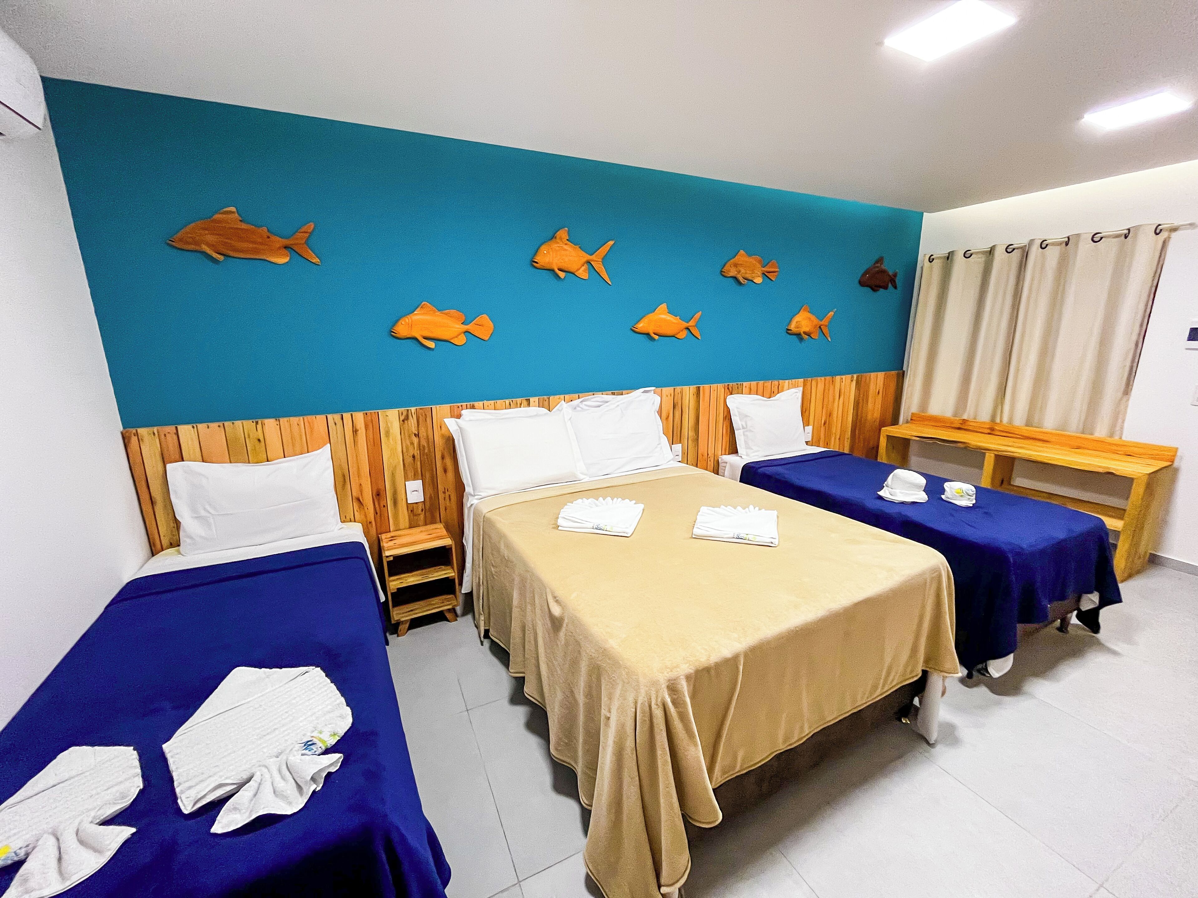 A hotel room with two beds, a wooden headboard, a small table, and a wall decorated with fish.