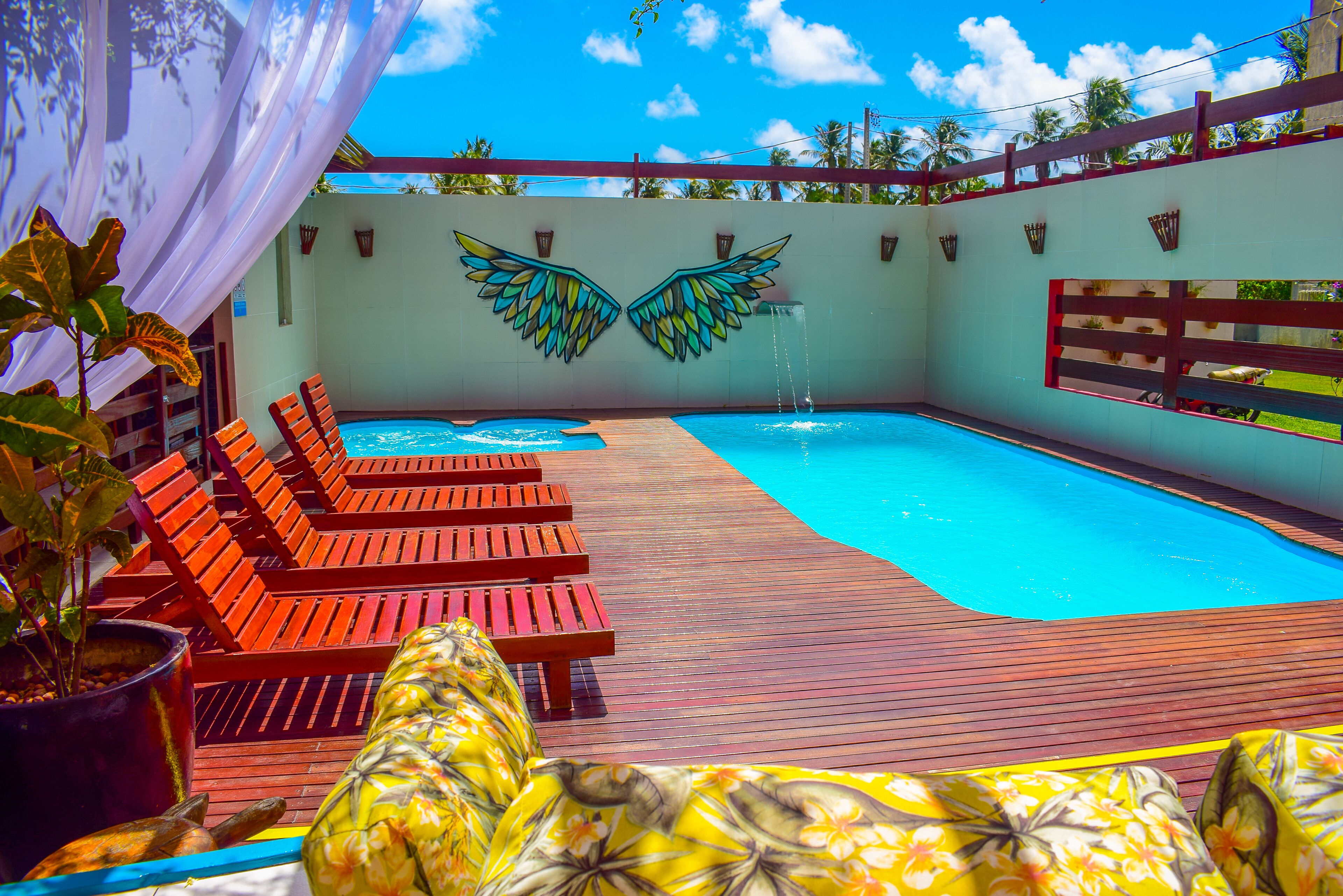 A swimming pool with wooden deck chairs and a mural of wings.