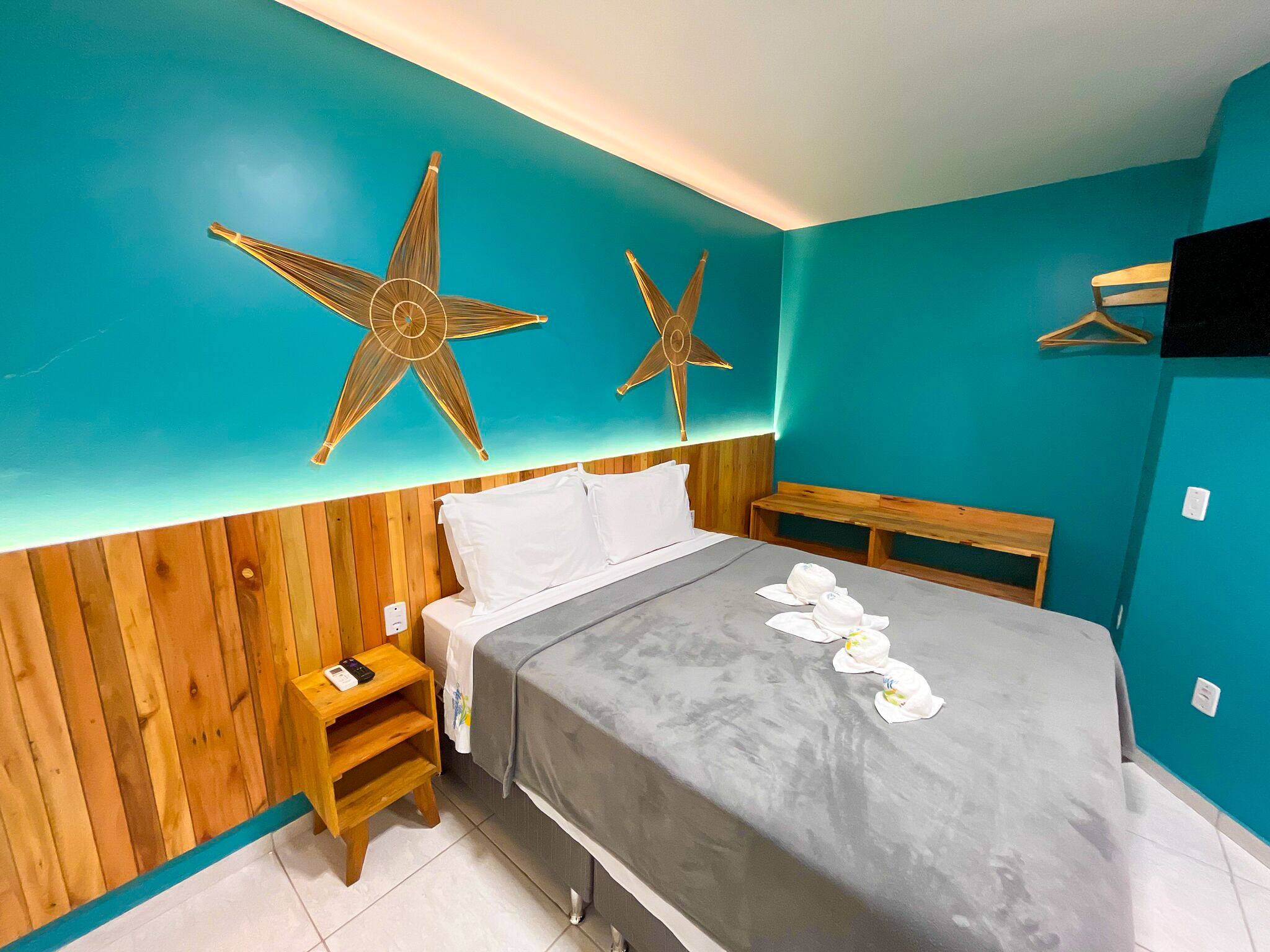 Hotelkamer met een bed, houten hoofdeinde, twee ster decoraties aan de muur, een nachtkastje met een telefoon, en een bankje.