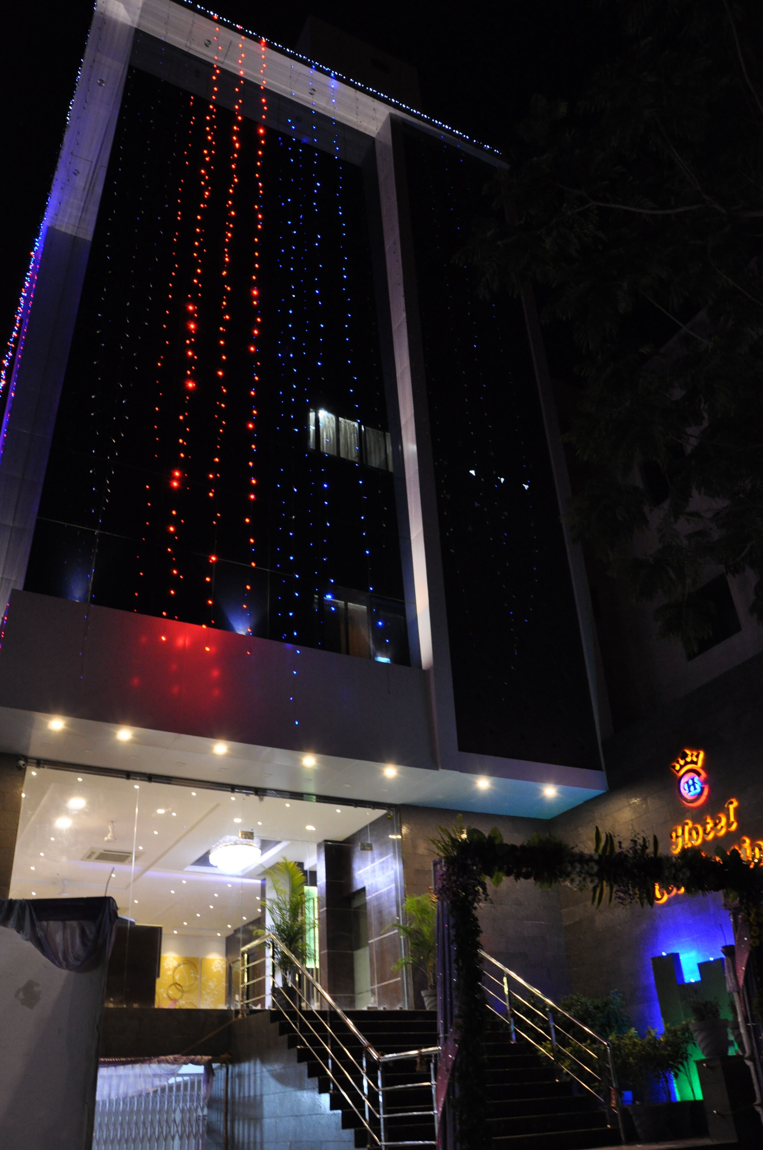 Entrada de un hotel con una escalera, una zona de recepción y un cartel con letras iluminadas.