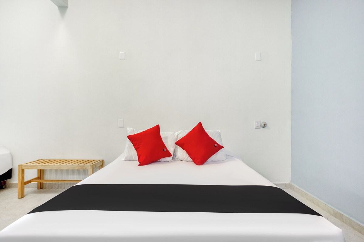 A neatly made bed with a black bedspread, two red pillows, and a wooden nightstand with a white lamp.