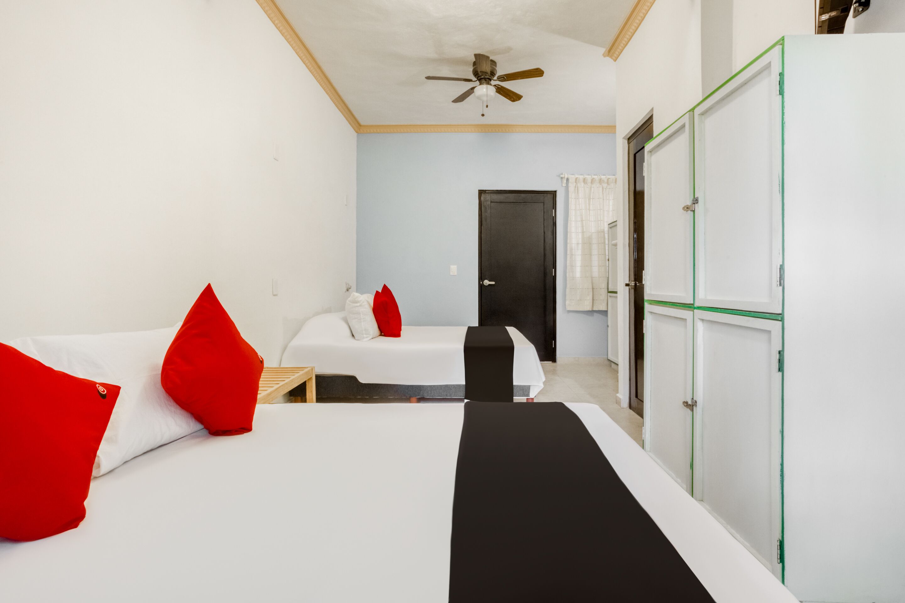 A room with two beds, a ceiling fan, a wardrobe, and a door.
