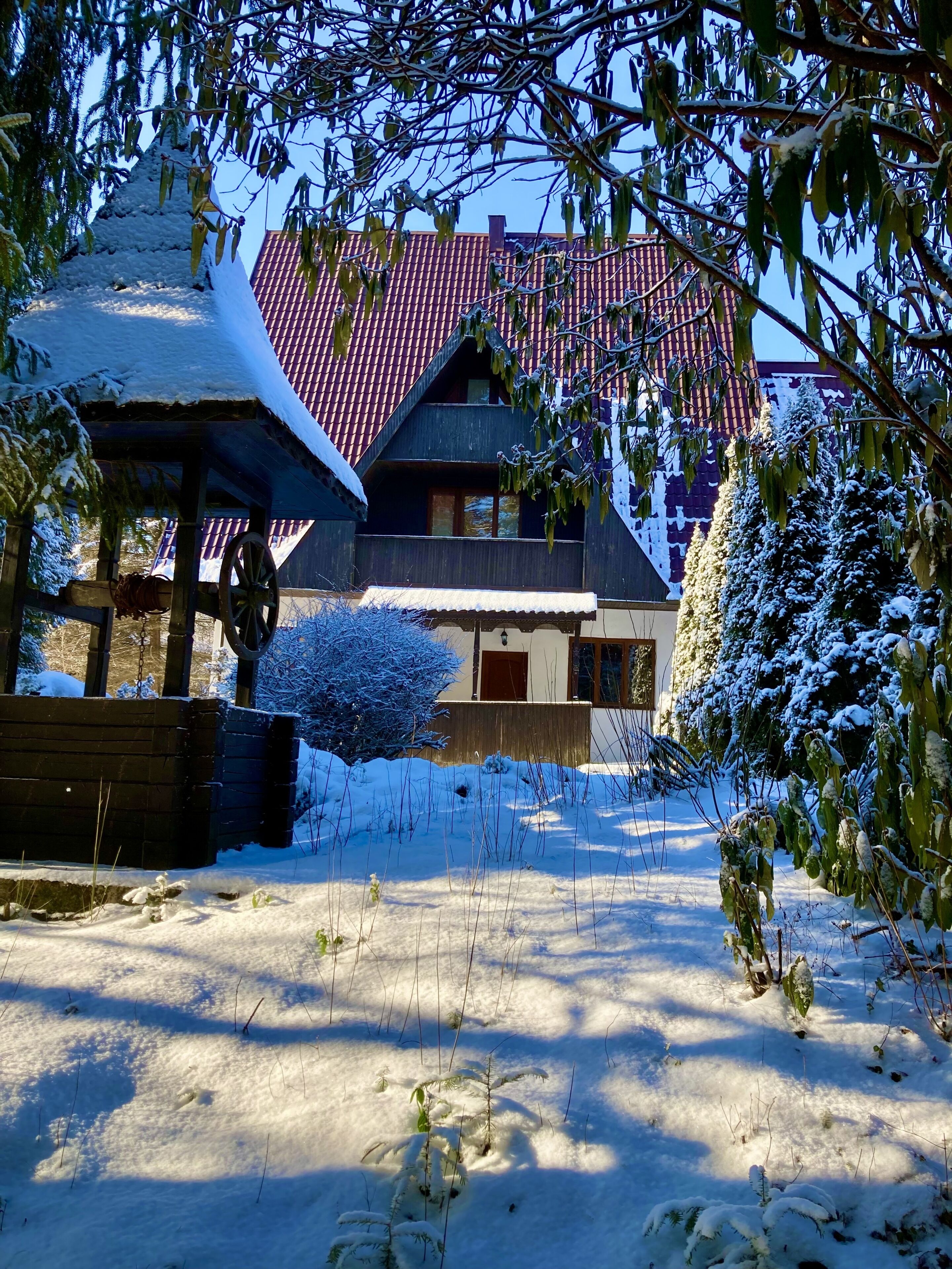 Una casa cubierta de nieve con techo rojo, un porche de madera y un patio cercado.