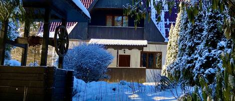 Una casa cubierta de nieve con techo rojo, un porche de madera y un patio cercado.