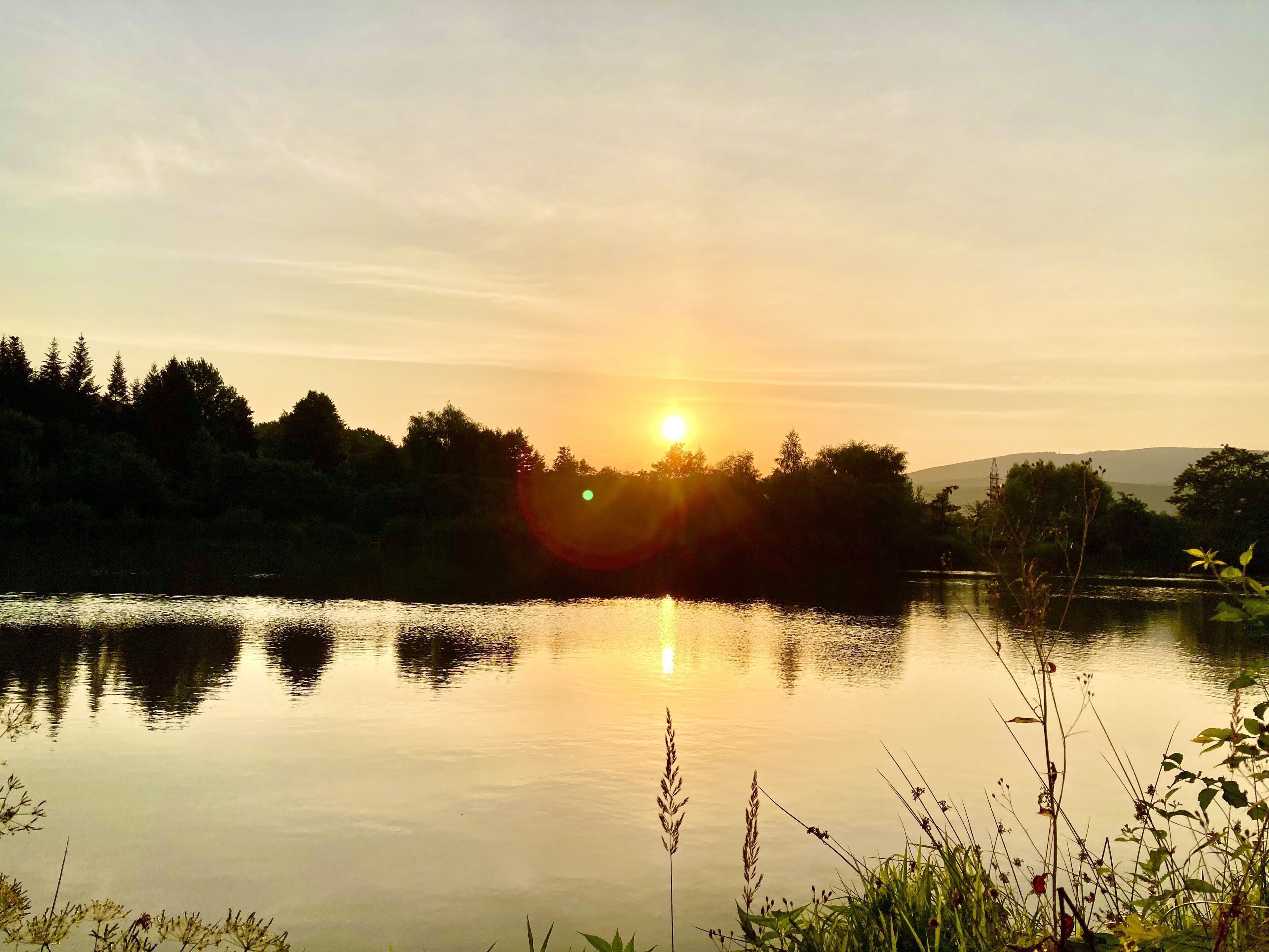 A calm lake at sunset with trees and hills in the background.